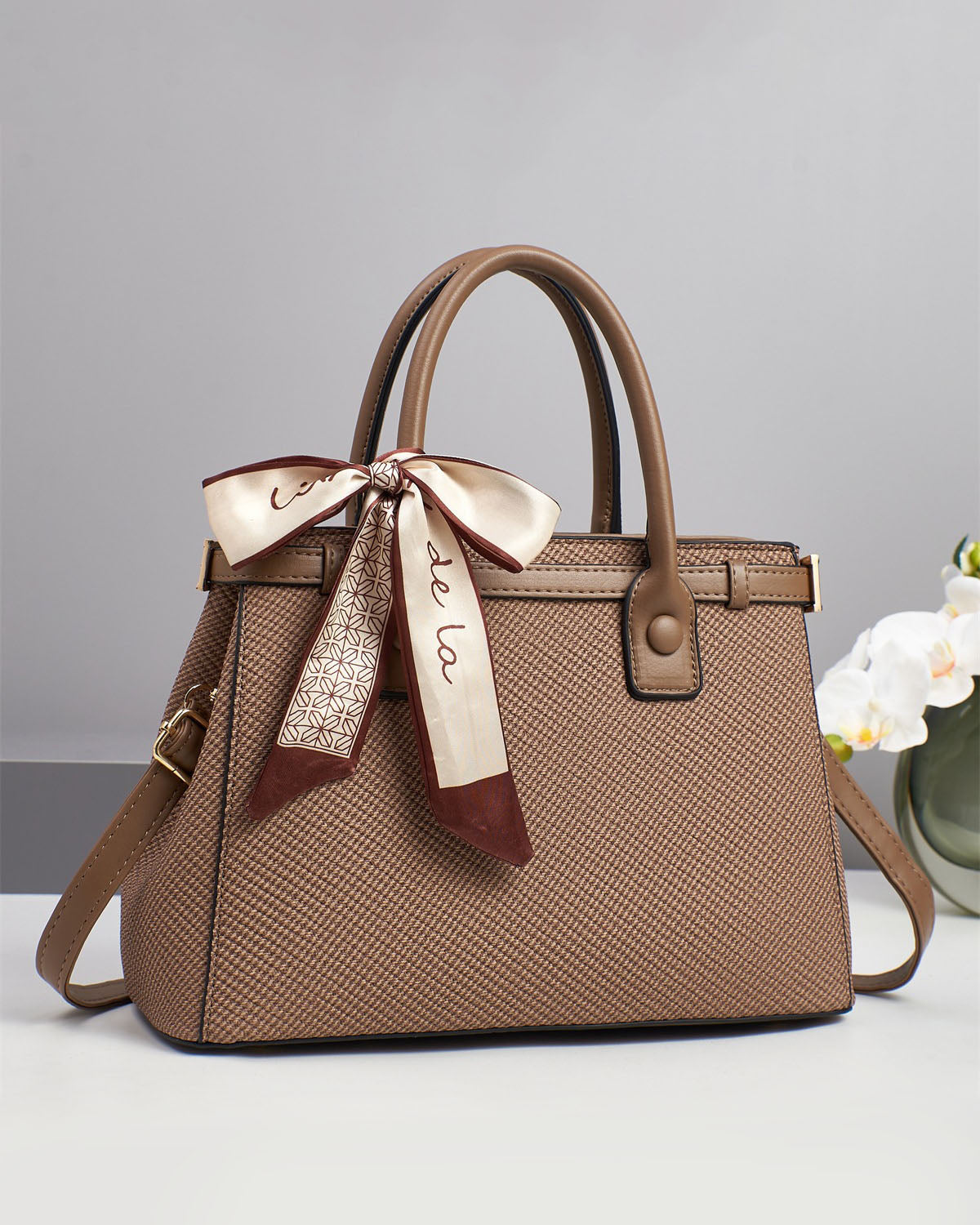 Bolso de mano con textura y un pañuelo de seda atado al asa.