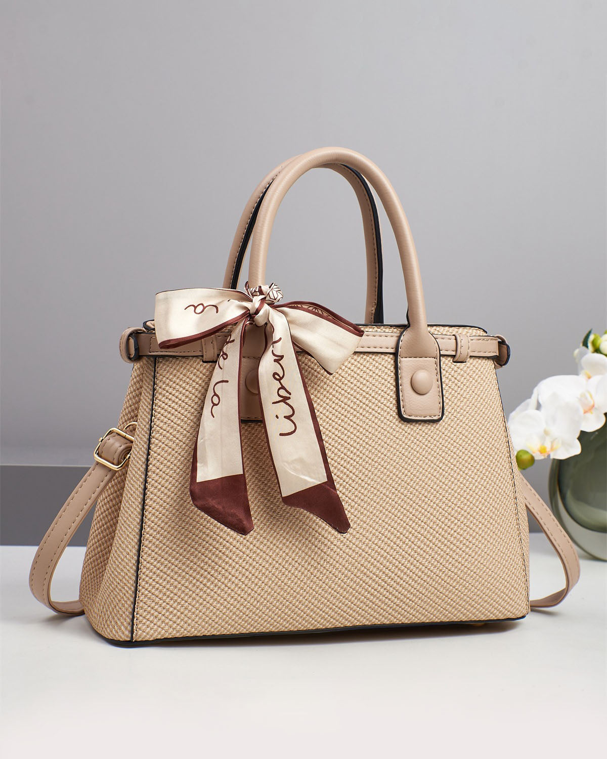 Bolso de mano con textura y un pañuelo de seda atado al asa.
