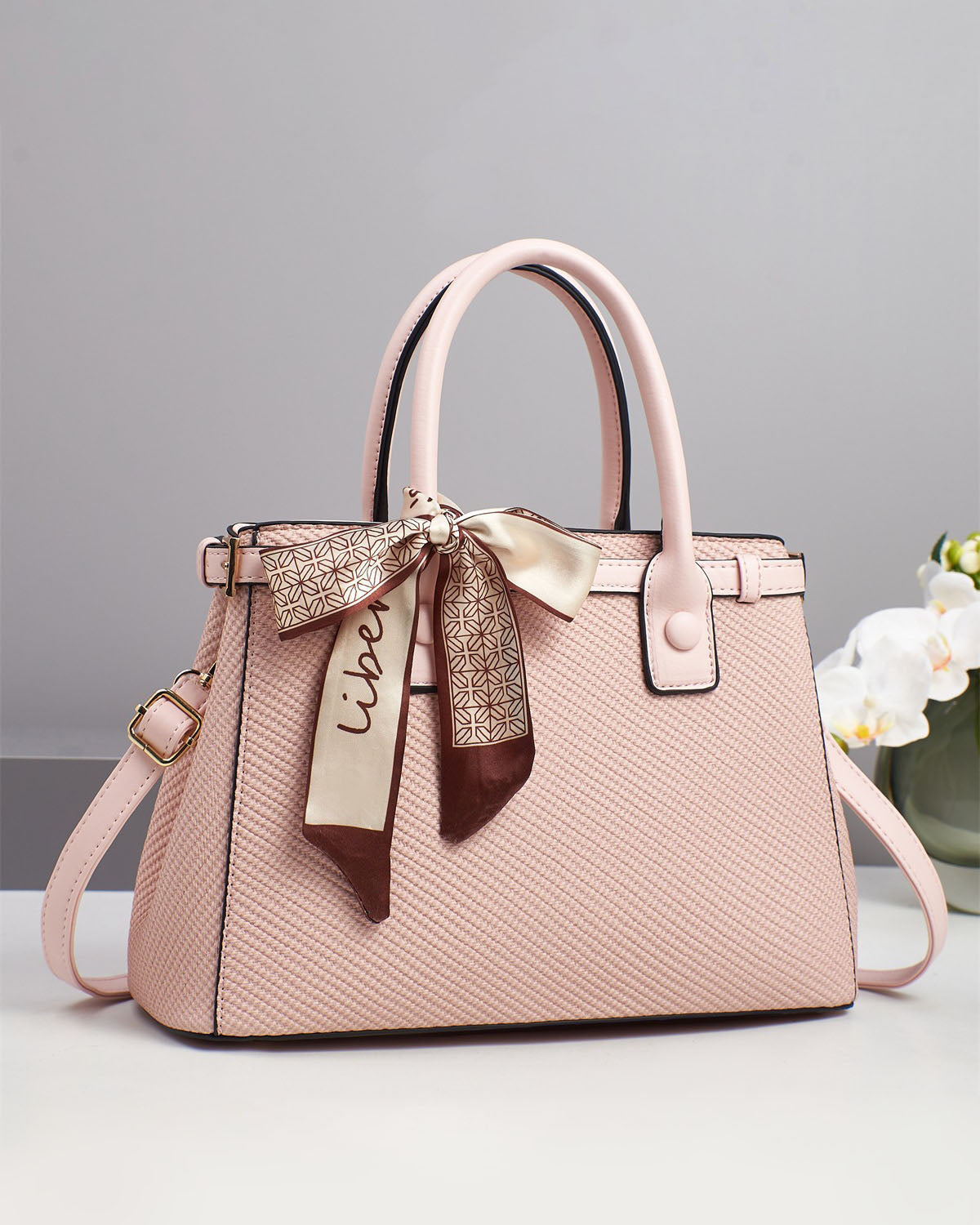 Bolso de mano con textura y un pañuelo de seda atado al asa.