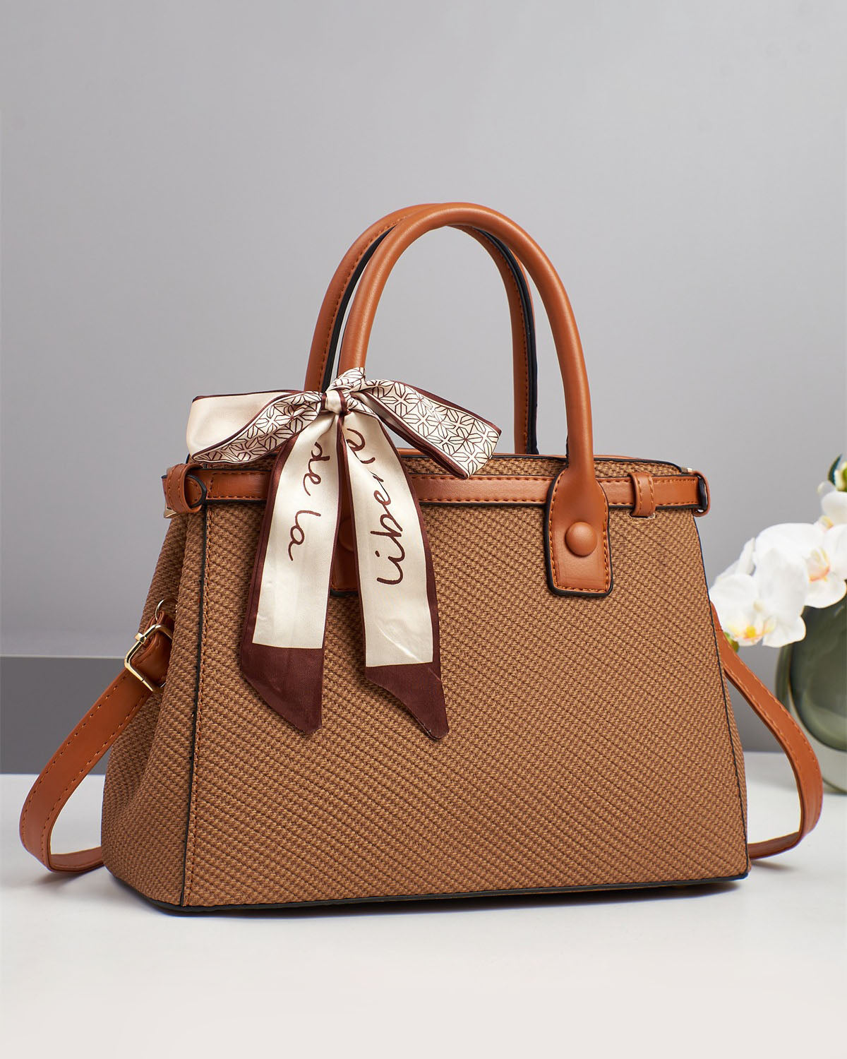 Bolso de mano con textura y un pañuelo de seda atado al asa.