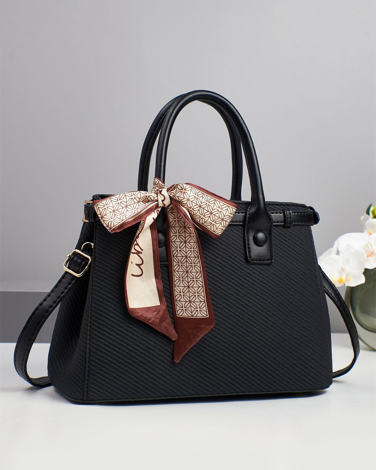 Bolso de mano con textura y un pañuelo de seda atado al asa.