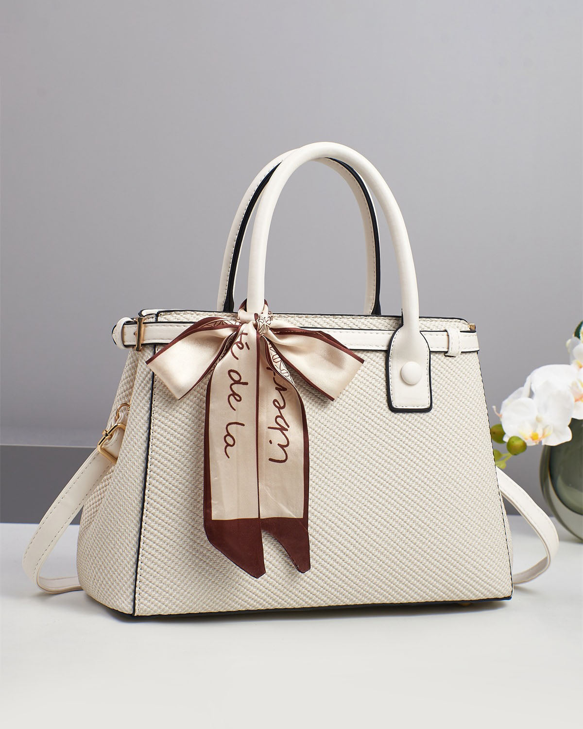 Bolso de mano con textura y un pañuelo de seda atado al asa.