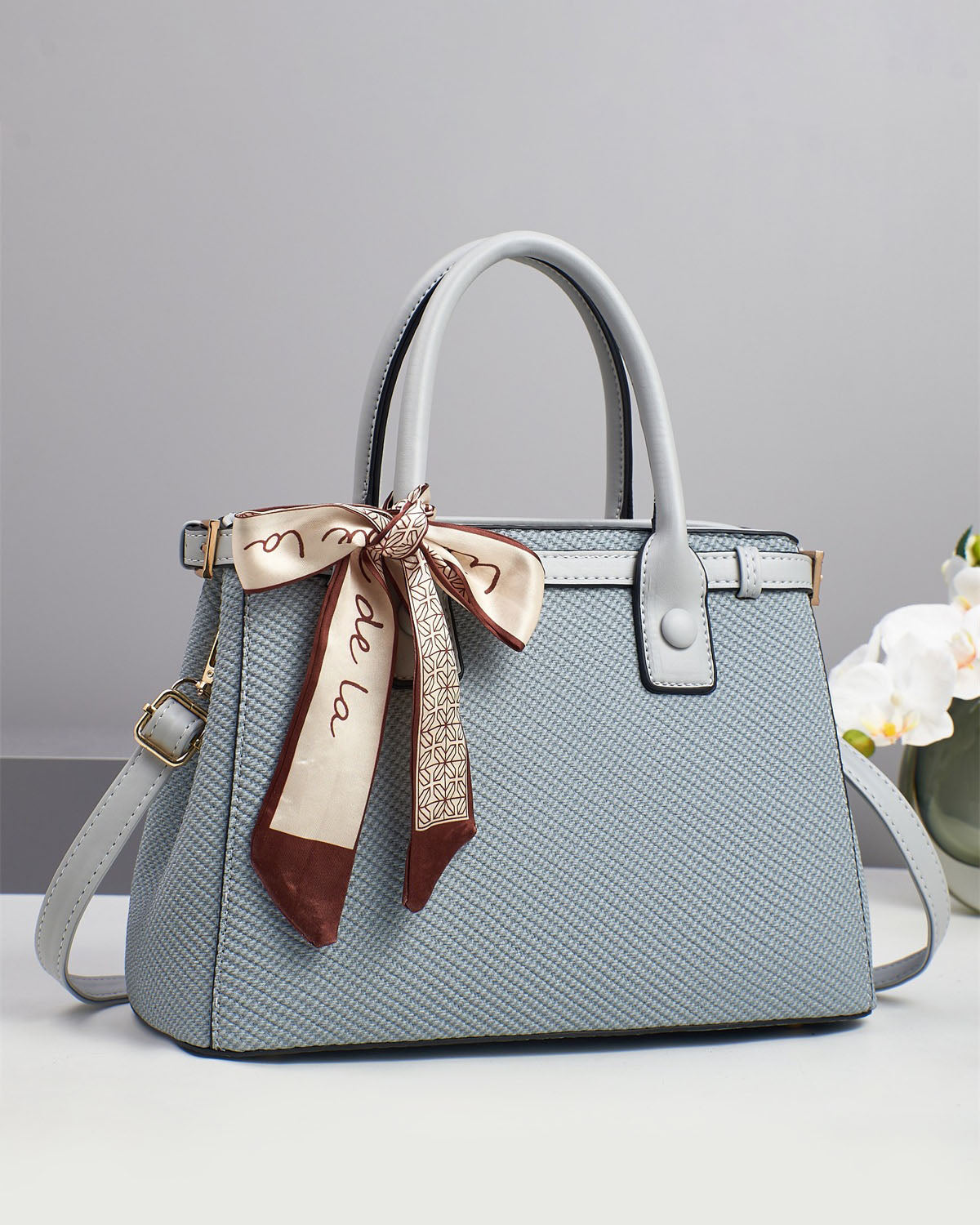 Bolso de mano con textura y un pañuelo de seda atado al asa.