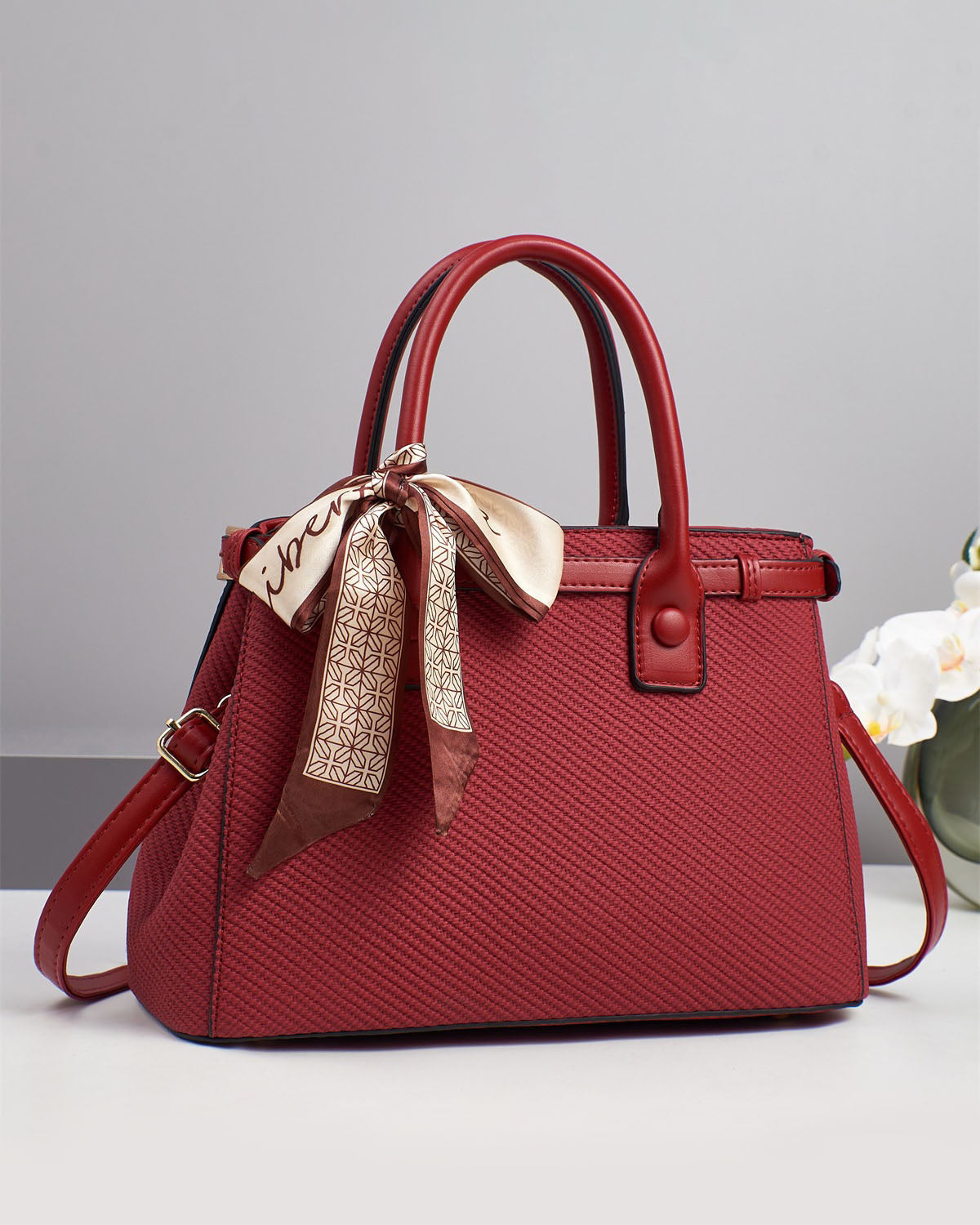 Bolso de mano con textura y un pañuelo de seda atado al asa.